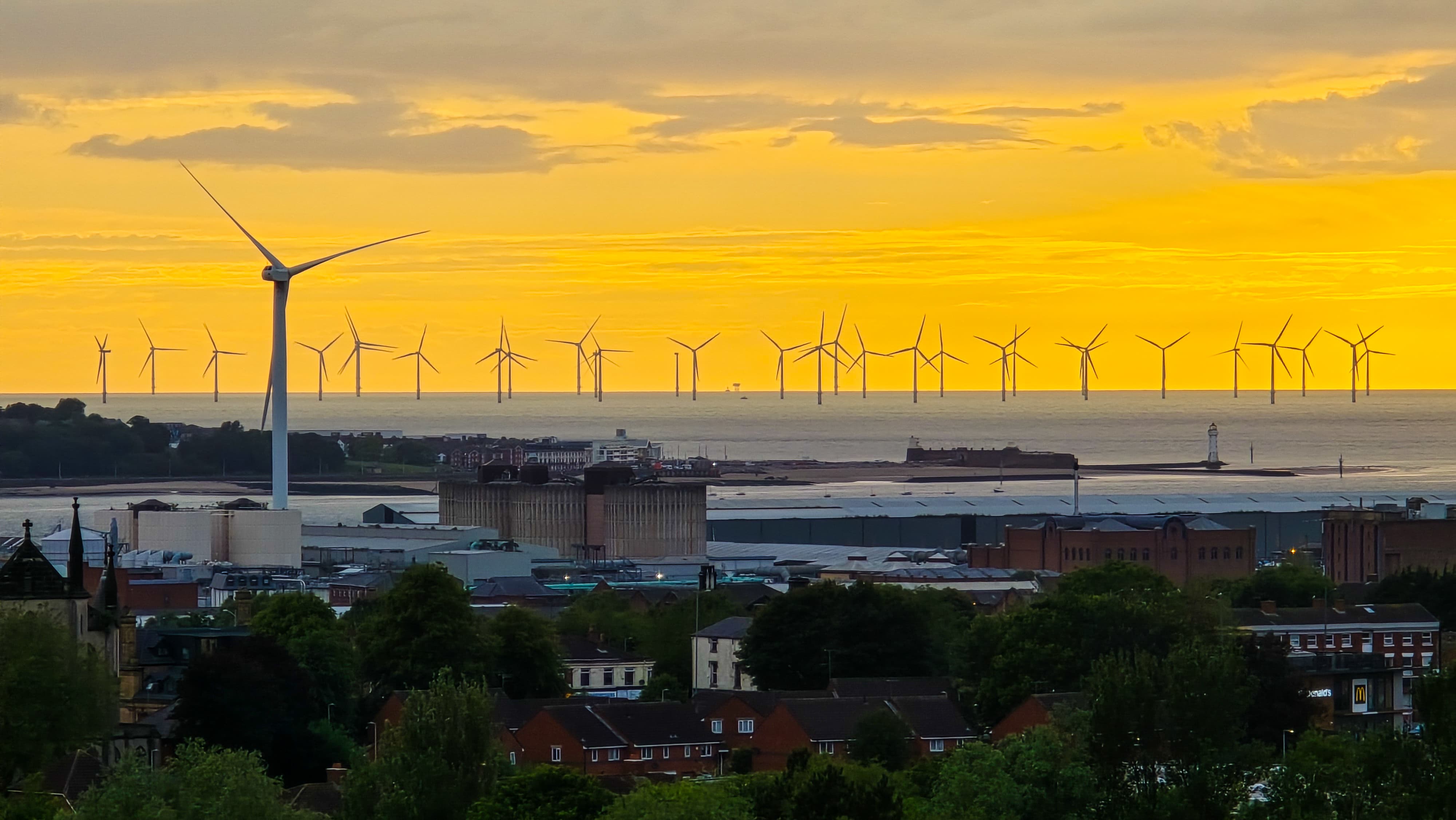 Golden hour view from Everton Park overlooking wind turbines across the sea and Liverpool cityscape.