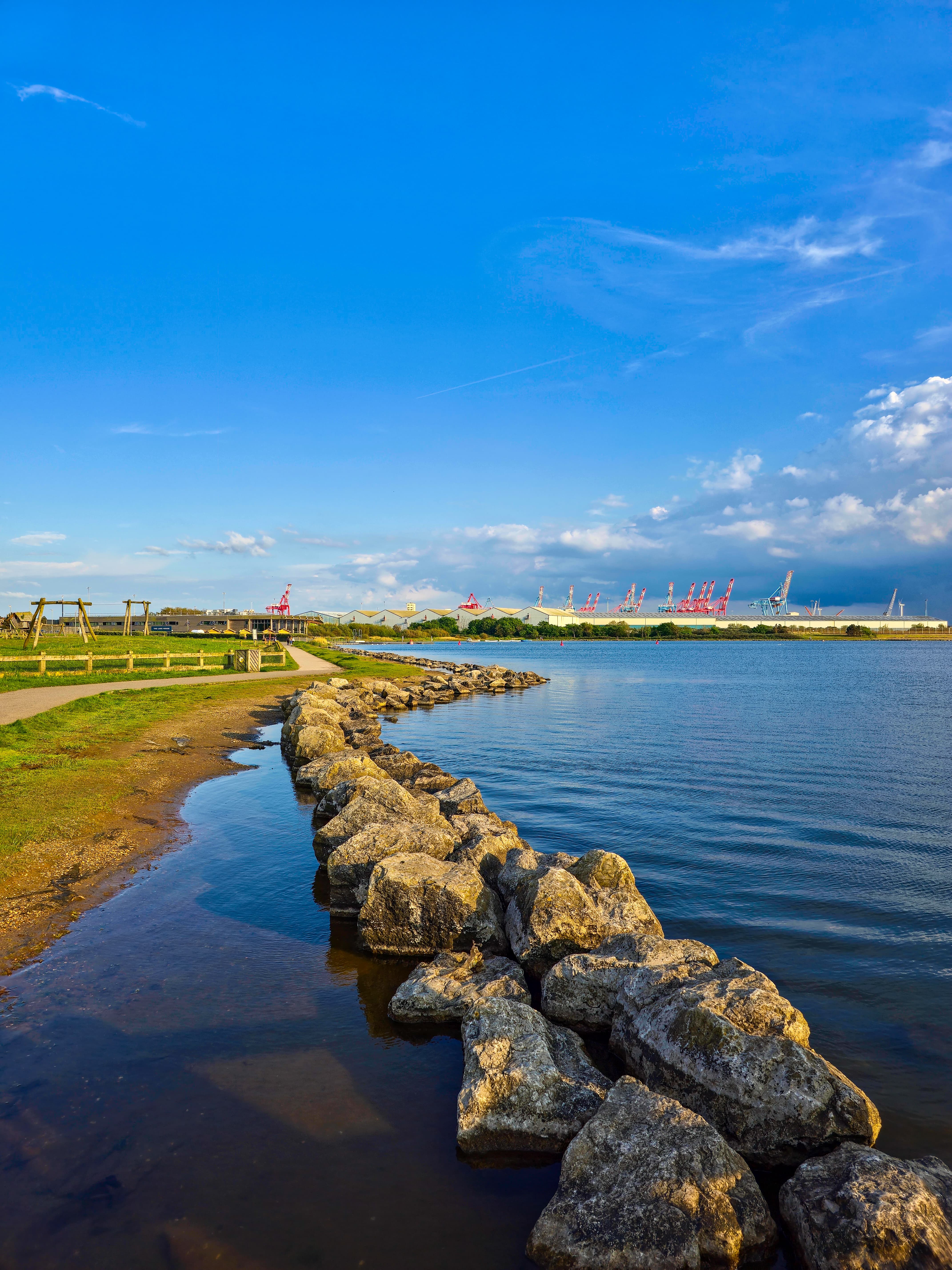 Stone trail curving along the calm waters of Crosby Beach under a vibrant blue sky