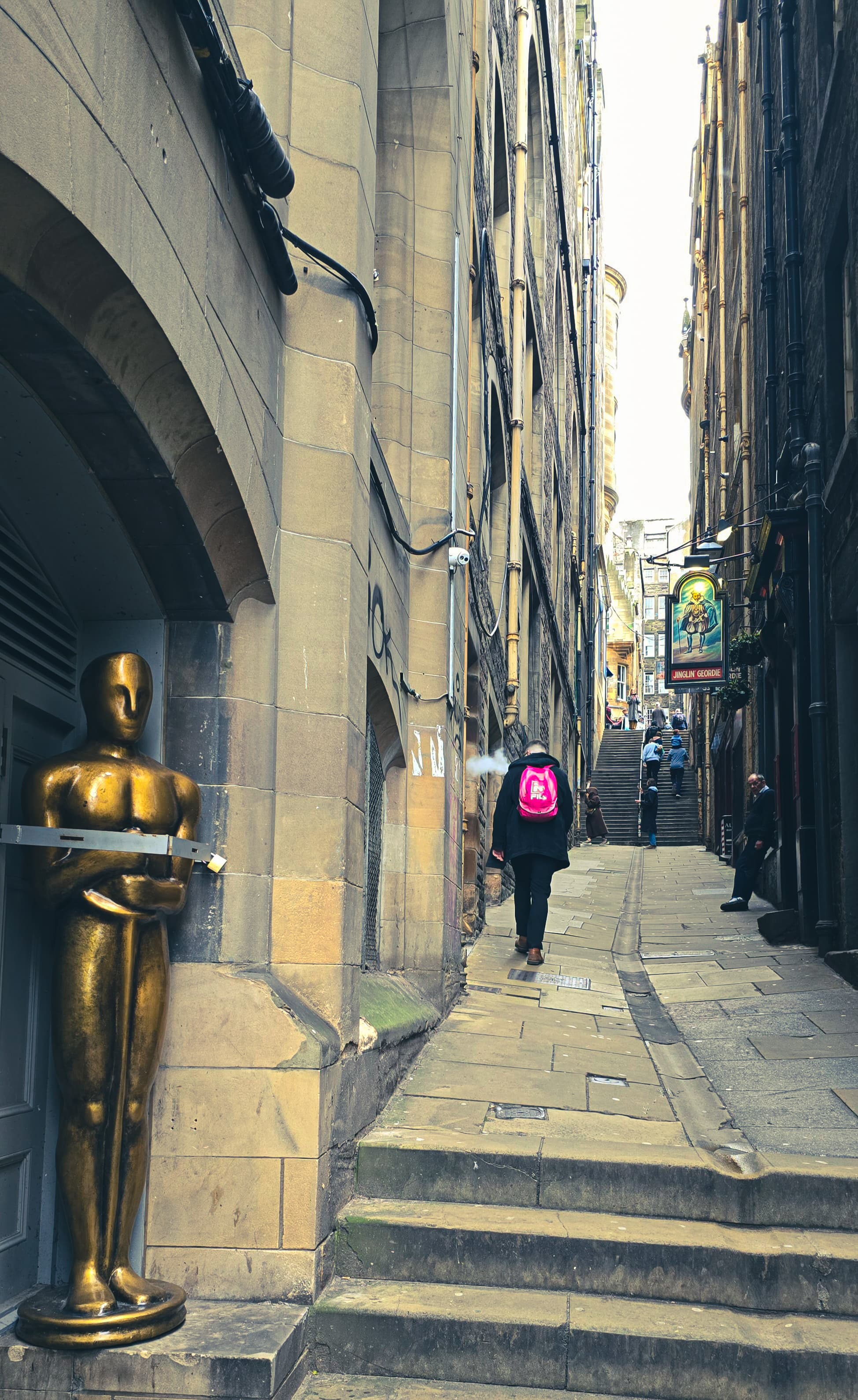 Gold statue at a narrow alley entrance in Edinburgh with people walking uphill.